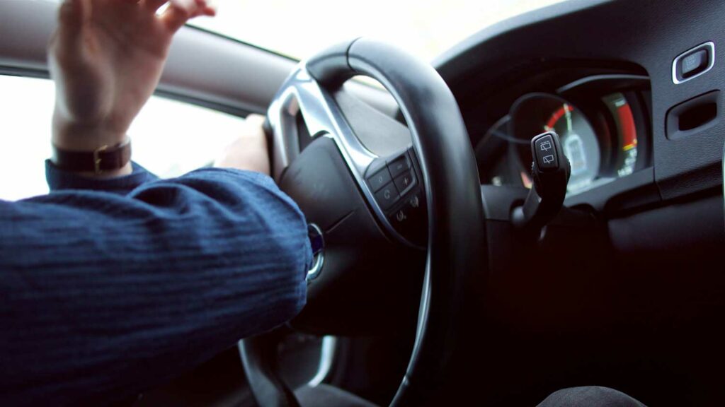 Close up of a man's hands on a steering wheel appear to swerve to avoid an accident